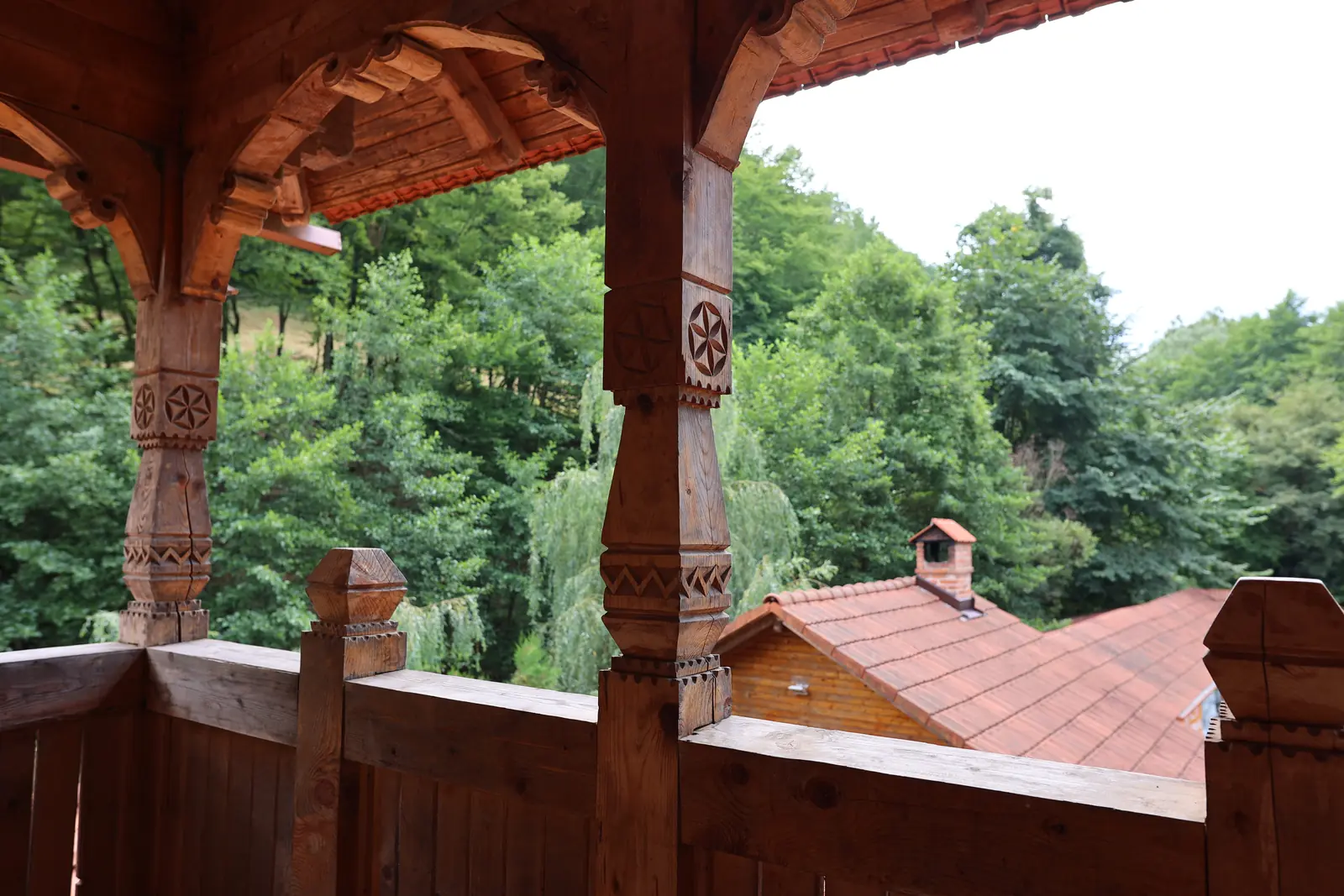 Stâlpi sculptați pe balconul de lemn, cu pădurea în fundal