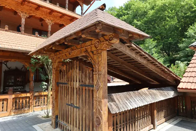 Poartă de lemn sculptată cu acoperiș de șindrilă în curtea pensiunii