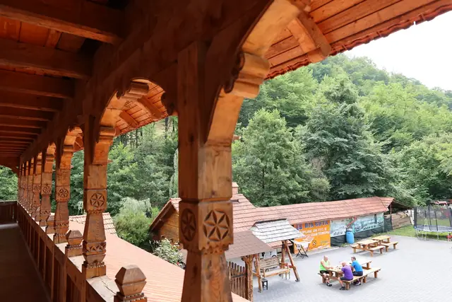 Pridvor cu arcade din lemn sculptat și vedere spre curtea pensiunii