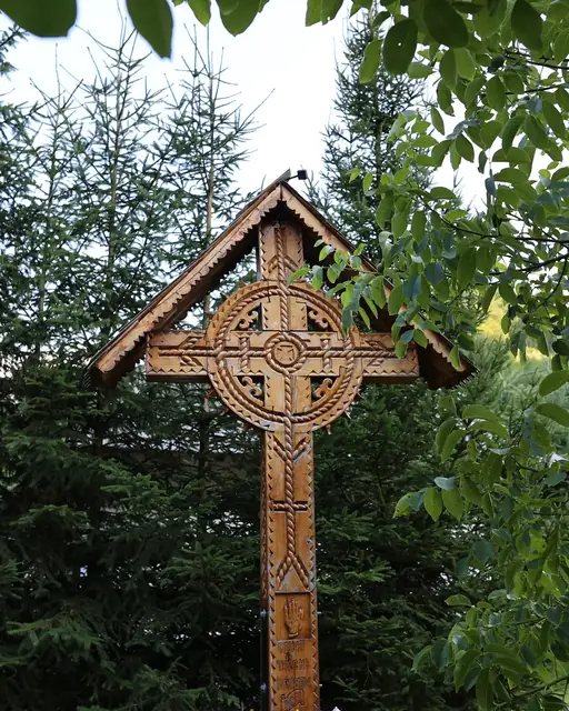 Troiță din lemn sculptat între brazii din grădina pensiunii
